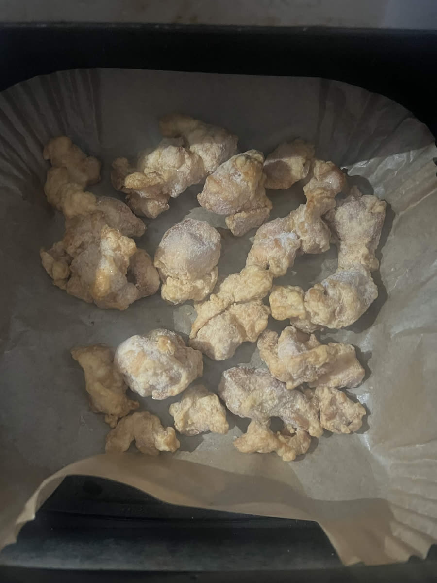 Frozen battered chicken pieces in a single layer on a parchment liner in an air fryer basket, still pale and frosted