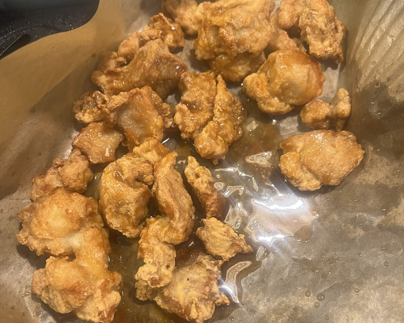 Battered chicken pieces, golden and crisp, on a parchment liner in an air fryer basket with orange sauce poured over them